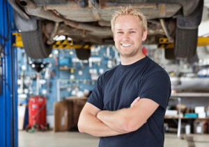 Portrait of cheerful young mechanic with arms crossed standing in his auto repair shop